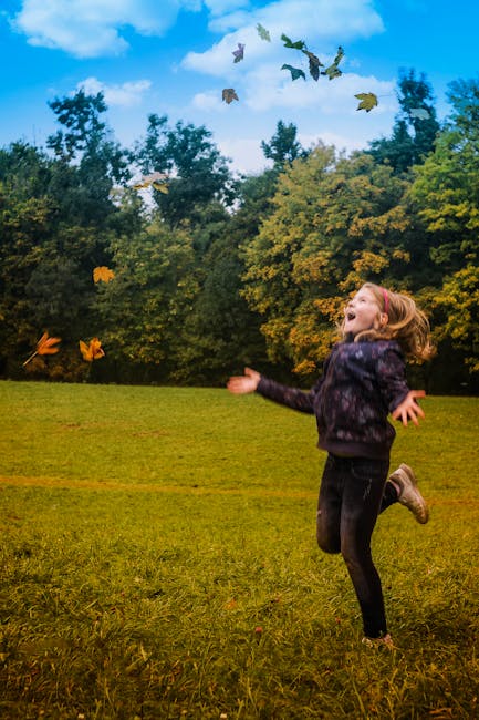 A young girl joyfully plays in a park, throwing autumn leaves in the air.